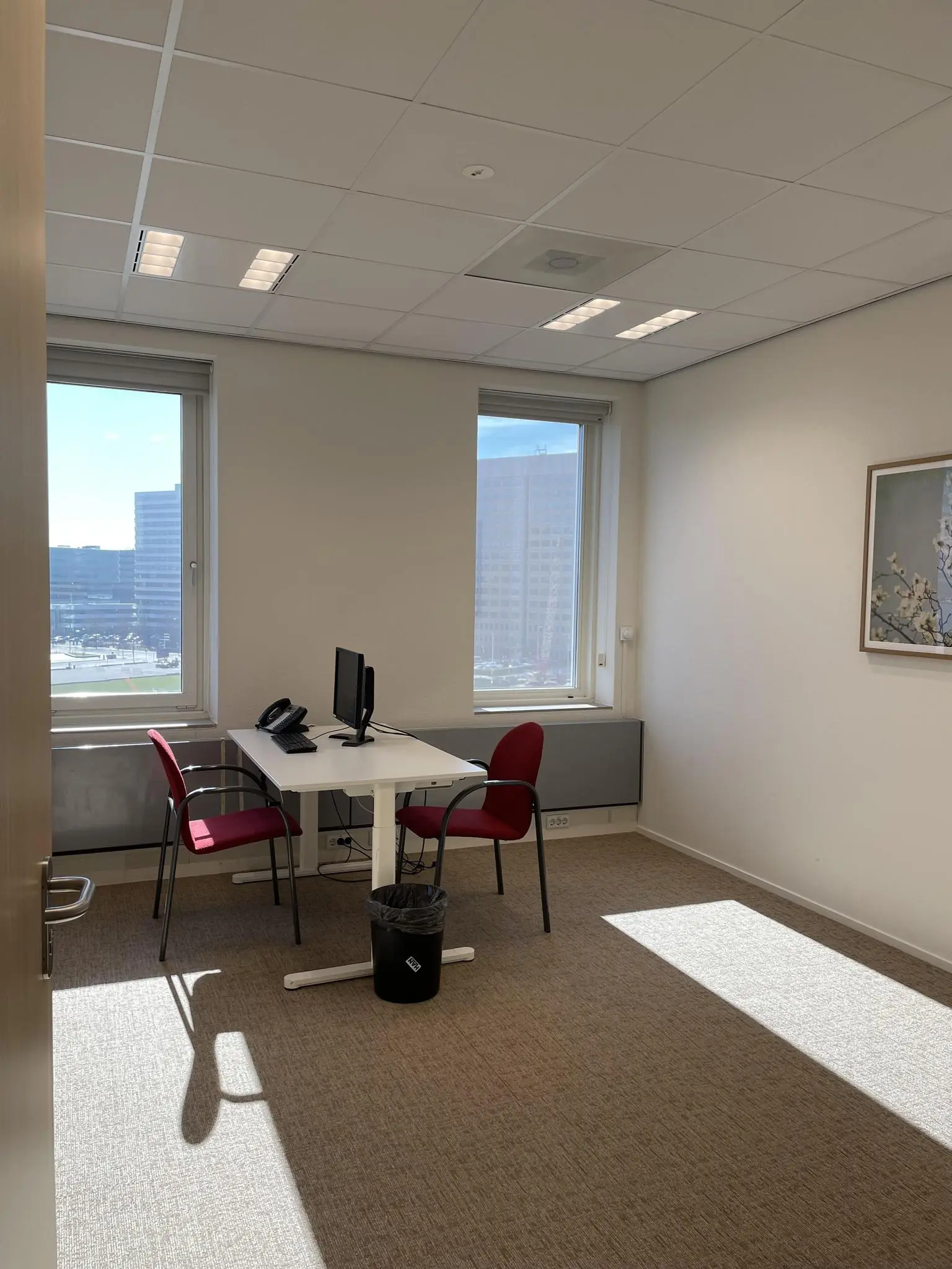 Klein kantoor met twee stoelen, een bureau met computer en uitzicht op de Johan Cruijff Boulevard.